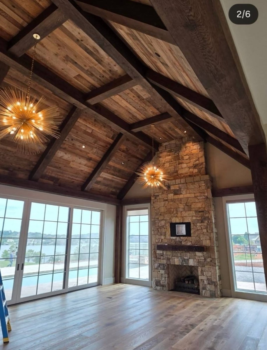 Vaulted great room with reclaimed wood ceiling, exposed beams, and stone fireplace